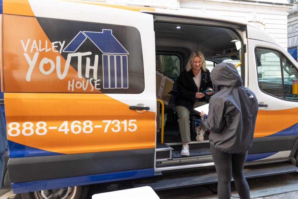 Katie Coulter sits inside of a van, talking to someone else who is holding a clipboard.
