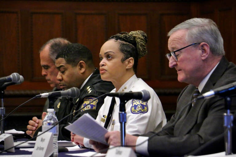 A row of people sit at a table with microphones in front of them.