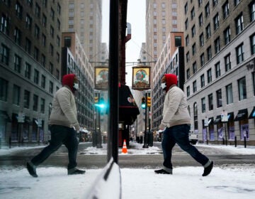 A person, reflected in a window while wearing a face mask as a precaution against the coronavirus, walks during a winter storm in Philadelphia