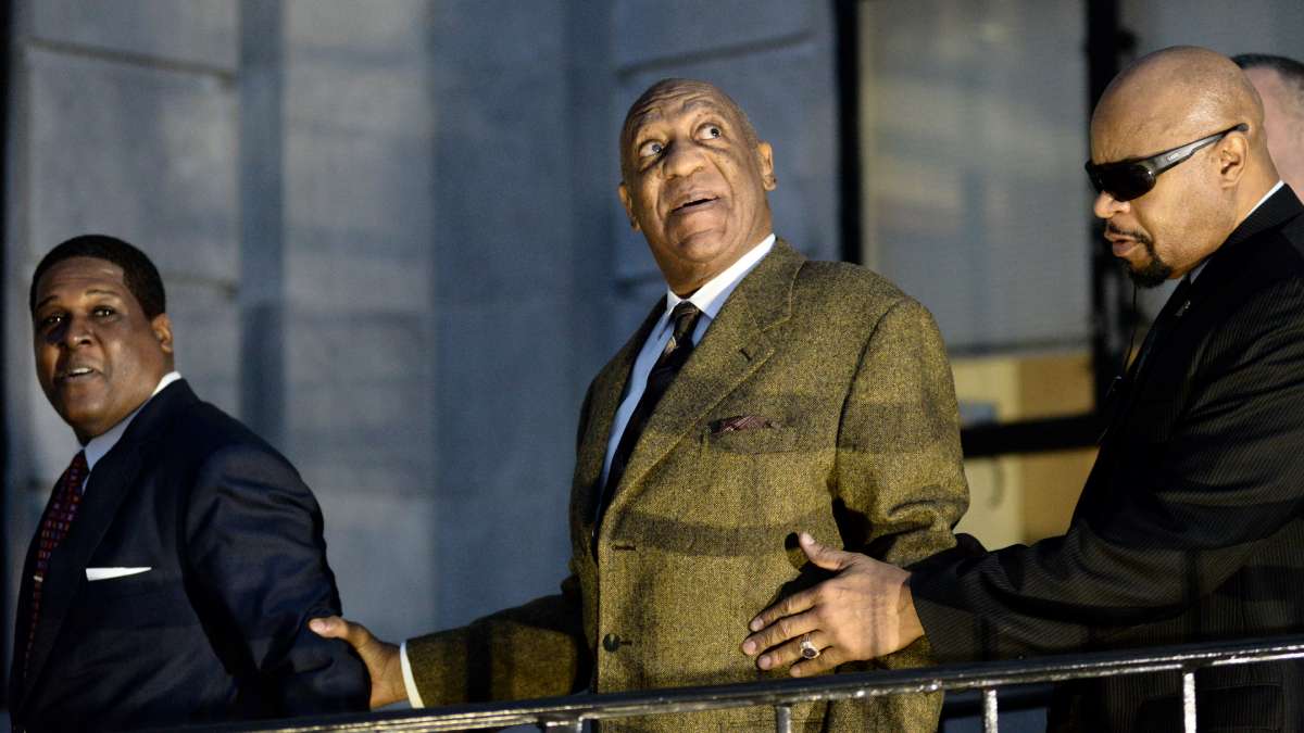 The spotlights of rolling cameras hit Bill Cosby's face as he looks up at the media helicopters above him seconds after he leaves Montgomery County Courthouse