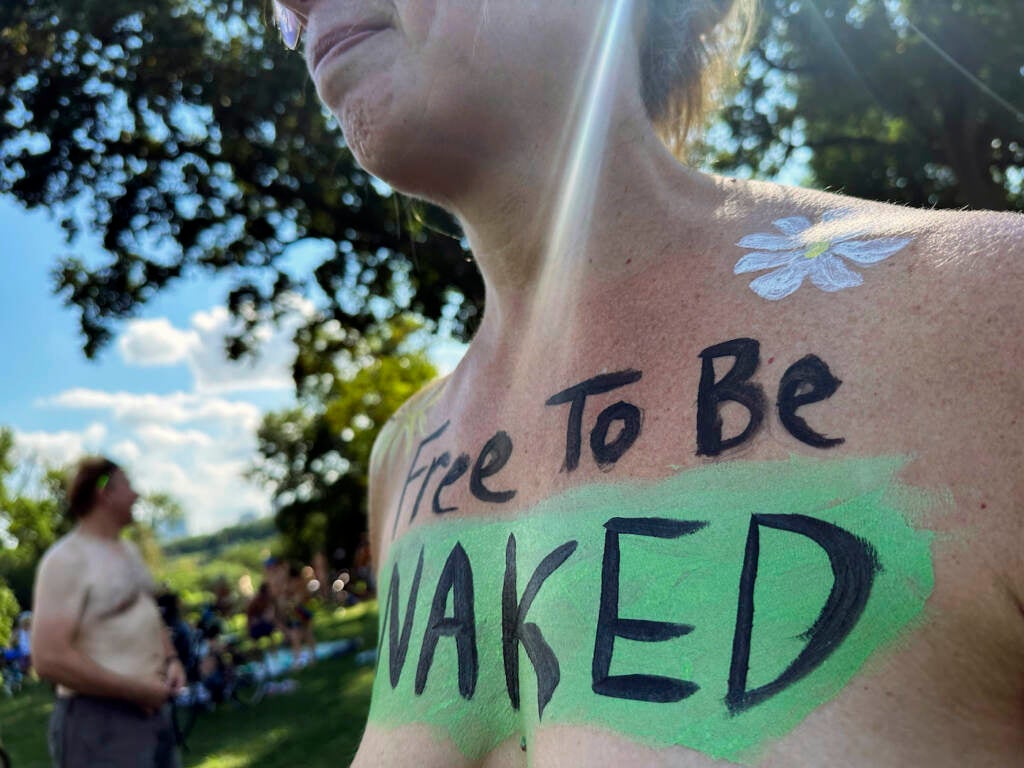 A woman with the phrase 'Free To Be Naked' written across her bare chest.